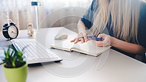 Girl holds a spartphone in her hand and takes notes in her notebook