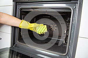 A girl holds a sponge in her hand against the background of an oven. Concept for cleaning electric ovens in the kitchen