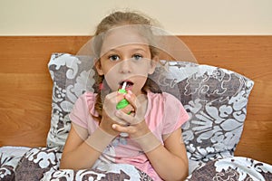 The girl holds a spray and irrigates their throats while sitting in bed. Self-treatment photo