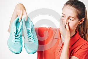 Girl holds stinky sneakers and closes her nose