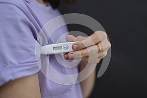 Girl holds a thermometer under the armpit. She`s going to measure the temperature. The concept of self-monitoring and self-testin