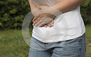 The girl holds on to the belly with both hands on the street, on a green background. Stomach upset or pain during menstruation