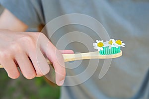 The girl holds a toothbrush with chamomile in her hand. Selective focus on toothbrush and chamomile