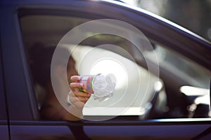 Girl holds trash outside the car window. A woman is about to throw waste out of a car. Environmental pollution