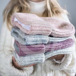 Girl holds winter knitted hats closeup on gray