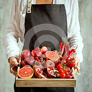 Girl holds wooden tray with fresh red vegetables and fruits on grey background. Healthy eating vegetarian concept.