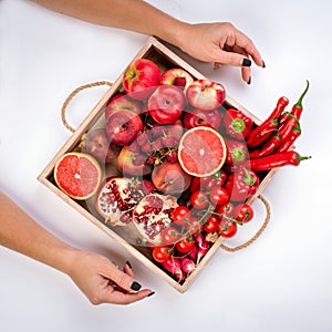 Girl holds wooden tray with fresh red vegetables and fruits on grey background. Healthy eating vegetarian concept.