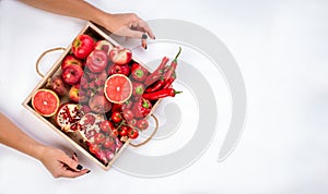 Girl holds wooden tray with fresh red vegetables and fruits on grey background. Healthy eating vegetarian concept.