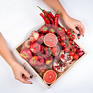 Girl holds wooden tray with fresh red vegetables and fruits on white background. Healthy eating vegetarian concept.