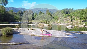 Girl holds yoga against peaceful river streaming among rocks