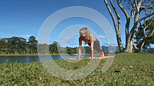 Girl Holds Yoga on Grass against River Landscape