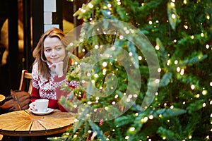 Girl in holiday sweater drinking coffee or hot chocolate in cafe decorated for Christmas