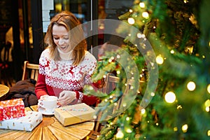 Girl in holiday sweater drinking coffee or hot chocolate in cafe decorated for Christmas