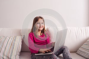 Girl at home sitting on sofa, playing with laptop