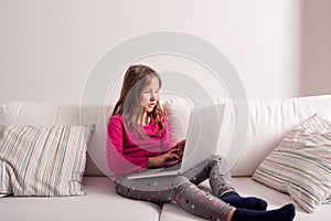 Girl at home sitting on sofa, playing with laptop