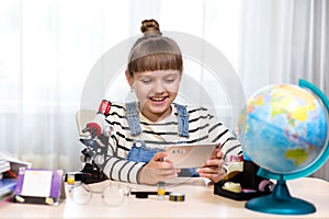 A girl at home at the table doing homework and using a smartphone. Home education, distance learning, home lessons