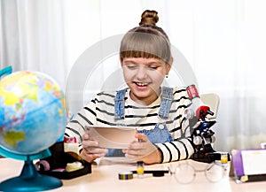 A girl at home at the table doing homework and using a smartphone. Home education, distance learning, home lessons