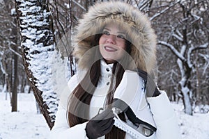A girl in a hood with white skates on a winter forest background