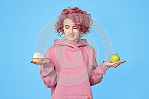 Girl in hoodie trying to choose between fresh green apple and sweet cupcake