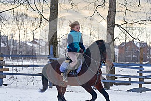 A girl on a horse jumps gallops. A girl trains riding a horse in a small paddock. A cloudy winter day