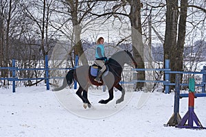 A girl on a horse jumps gallops. A girl trains riding a horse in a small paddock. A cloudy winter day