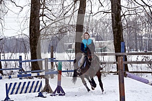 A girl on a horse jumps gallops. A girl trains riding a horse in a small paddock. A cloudy winter day