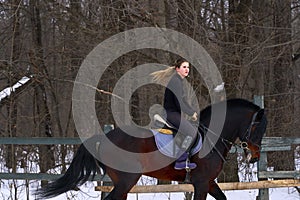 A girl on a horse jumps gallops. A girl trains riding a horse in a small paddock. A cloudy winter day