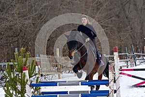 A girl on a horse jumps over the barrier. Training girl jockey riding a horse. A cloudy winter day