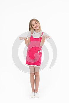 Girl in hot pink jumpsuit isolated on white background. Smiling kid wearing summer outfit. Child with hands in I don`t