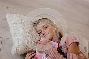 Girl hugging a Christmas gift box. smiling kid lying on a pillow and holding a present