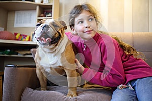 Girl hugging an English bulldog on a couch in the