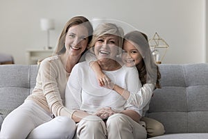 Girl hugging her granny sit on sofa with young mom