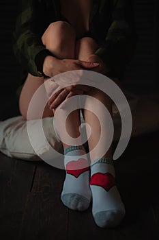 Girl hugs feet wearing white socks with red heart shape on wooden floor background. Love concept