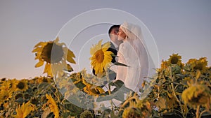 The girl hugs her beloved young man in a beautiful field of sunflowers. she`s wearing a beautiful white dress.