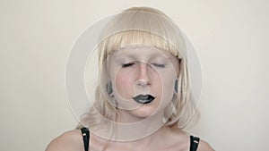 Girl in the image of albino with black lips and white eyes. Art beauty face. Picture taken in the studio on a white