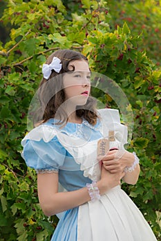 Girl in image of fairy tale heroine doubts and holding a glass bottle with a label drink me.