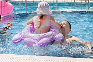 A girl with an inflatable circle and a boy play in the pool.