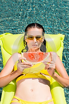 Girl on inflatable mattress with watermelon in pool on resort
