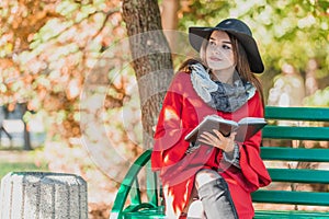 Girl inspired by nature sits on the bench in park writing a poem or song in a notebook.