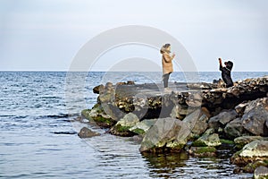 A girl in a jacket walks on the coast of the sea with a Rottweiler dog