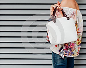 A girl in jeans and a fashionable colored blouse with a fashionable white handbag posing against a background of white