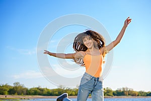 Girl in jeans and an orange t-shirt jumps against the sky