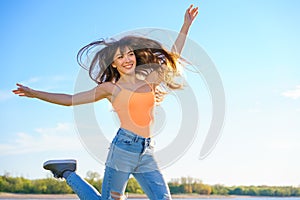 Girl in jeans and an orange t-shirt jumps against the sky