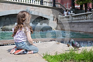 Girl in jeans sits near the fountain and feeding birds