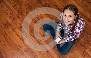 Girl in jeans sits on wooden floor and holding a smartphone. Concept of teenage life and gadgets. Top view with copy space.