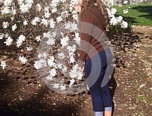 Girl with jeans standing in a garden smithing the white flowers