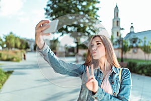 Girl in jeans, in summer in city park, holding smartphone in her hand, taking pictures, selfie, video call online