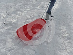 Girl in jeans and wellington boots pulling a red sledge in the snow