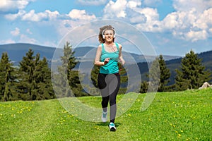 Girl jogging on trail in mountains on field with grass in summer sunny day.