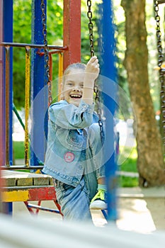 Girl joyfully and fervently laughs sitting on a hanging ladder in the playground